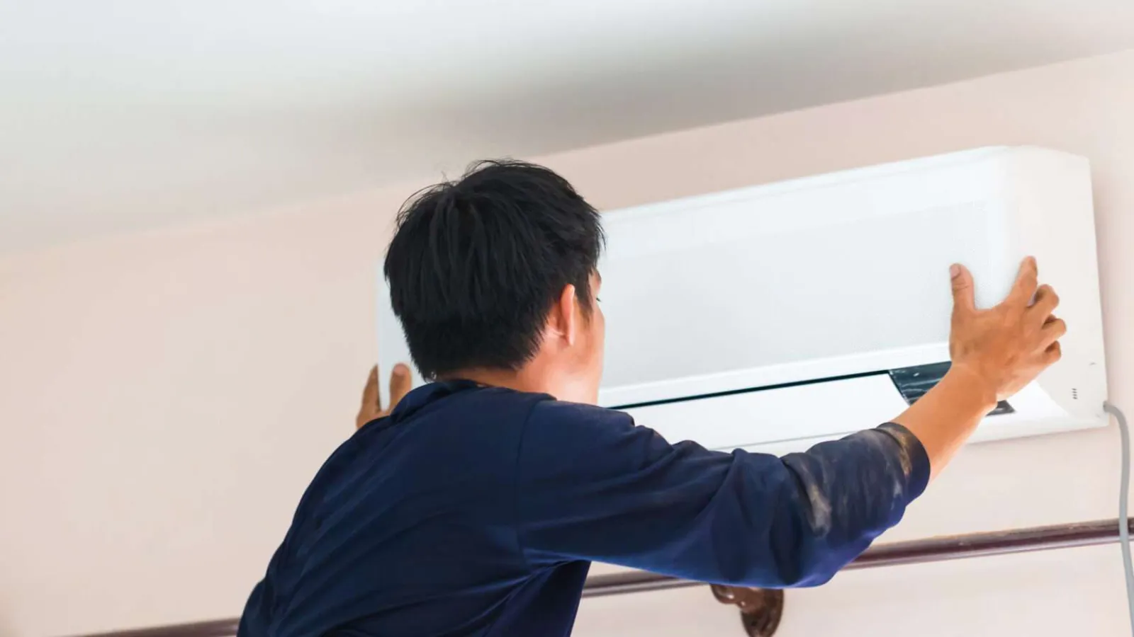 Technician installing or servicing a wall-mounted air conditioner unit indoors in a residential setting.