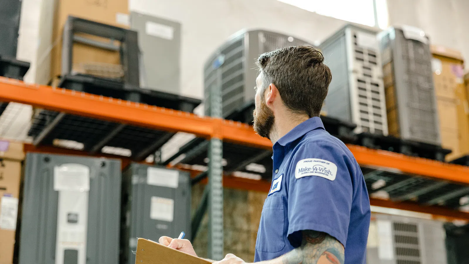 Warehouse worker with clipboard inspecting inventory on high metal shelves in storage facility.