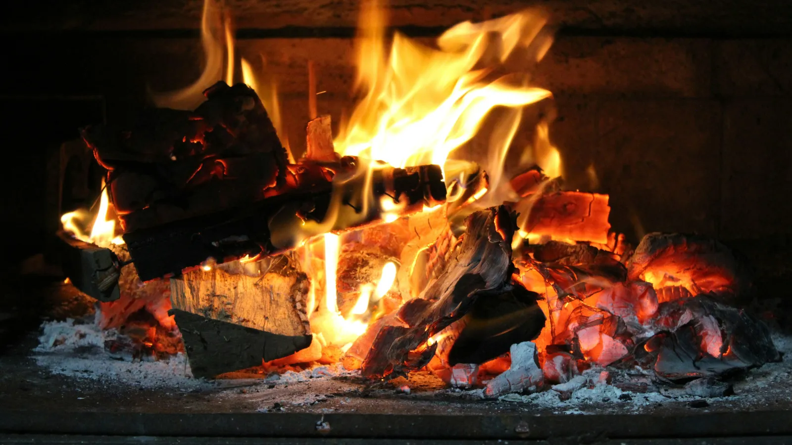 Cozy stone fireplace with a wooden mantle, burning fire, stacked firewood, and cushioned seating in rustic setting