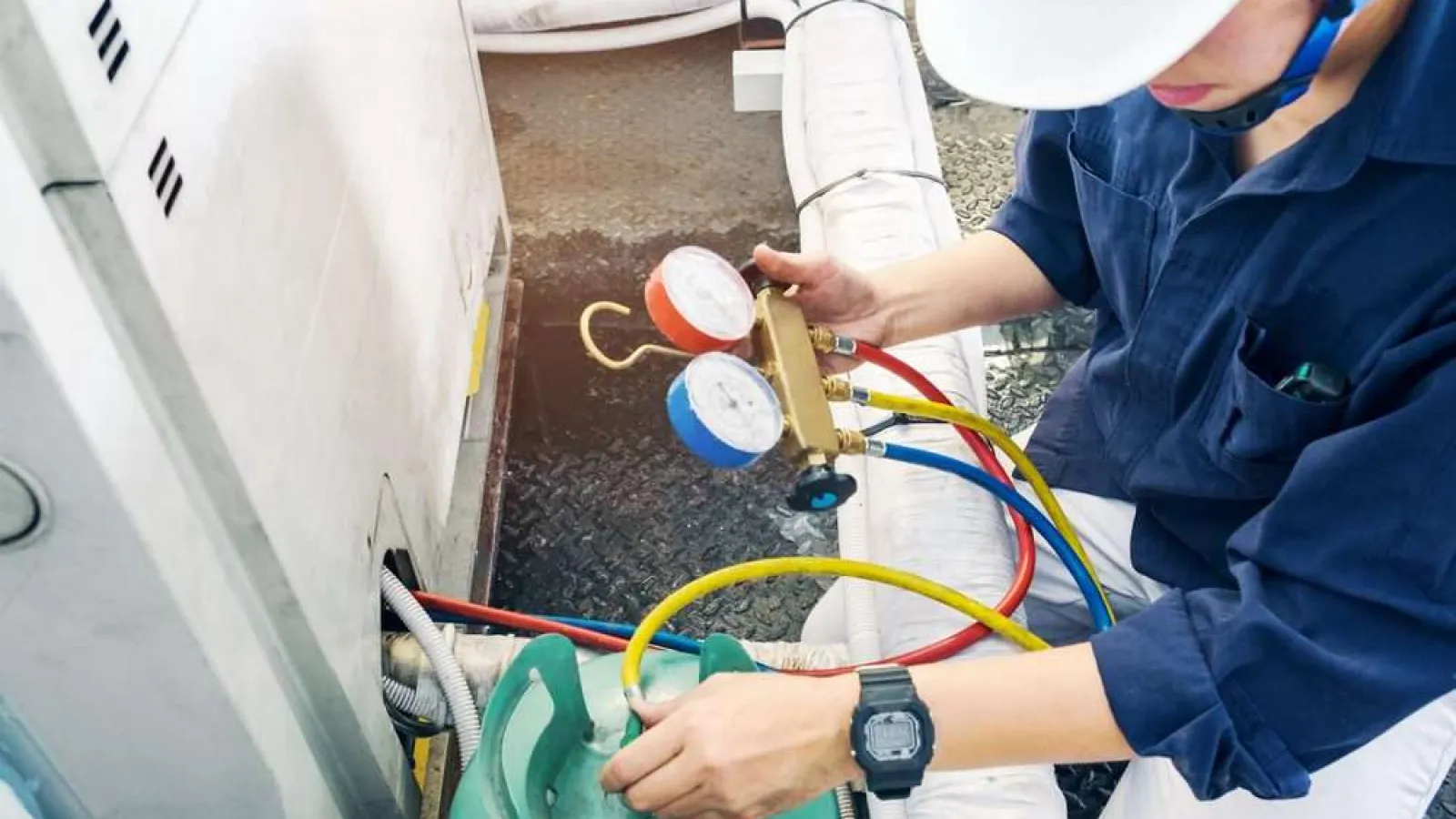 Technician with glasses inspecting and repairing an outdoor HVAC unit during daytime.