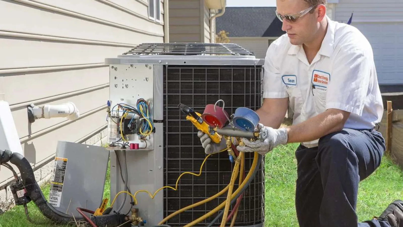 Technician in uniform repairing an outdoor air conditioning unit with gauges and hoses on green lawn.