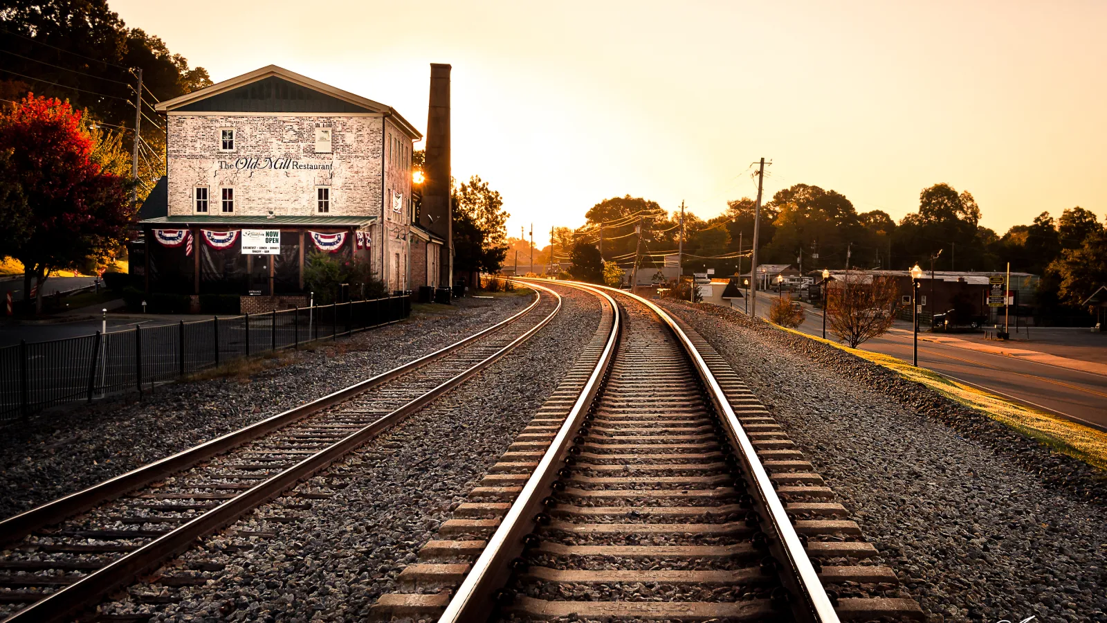Sunset over railroad tracks next to a historic restaurant building with warm golden light and autumn trees.