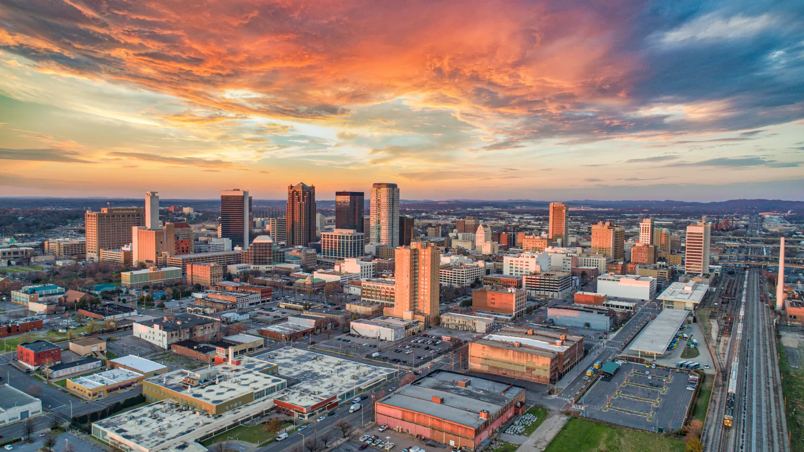 Aerial view of a modern city skyline at sunset with colorful dramatic clouds and buildings.