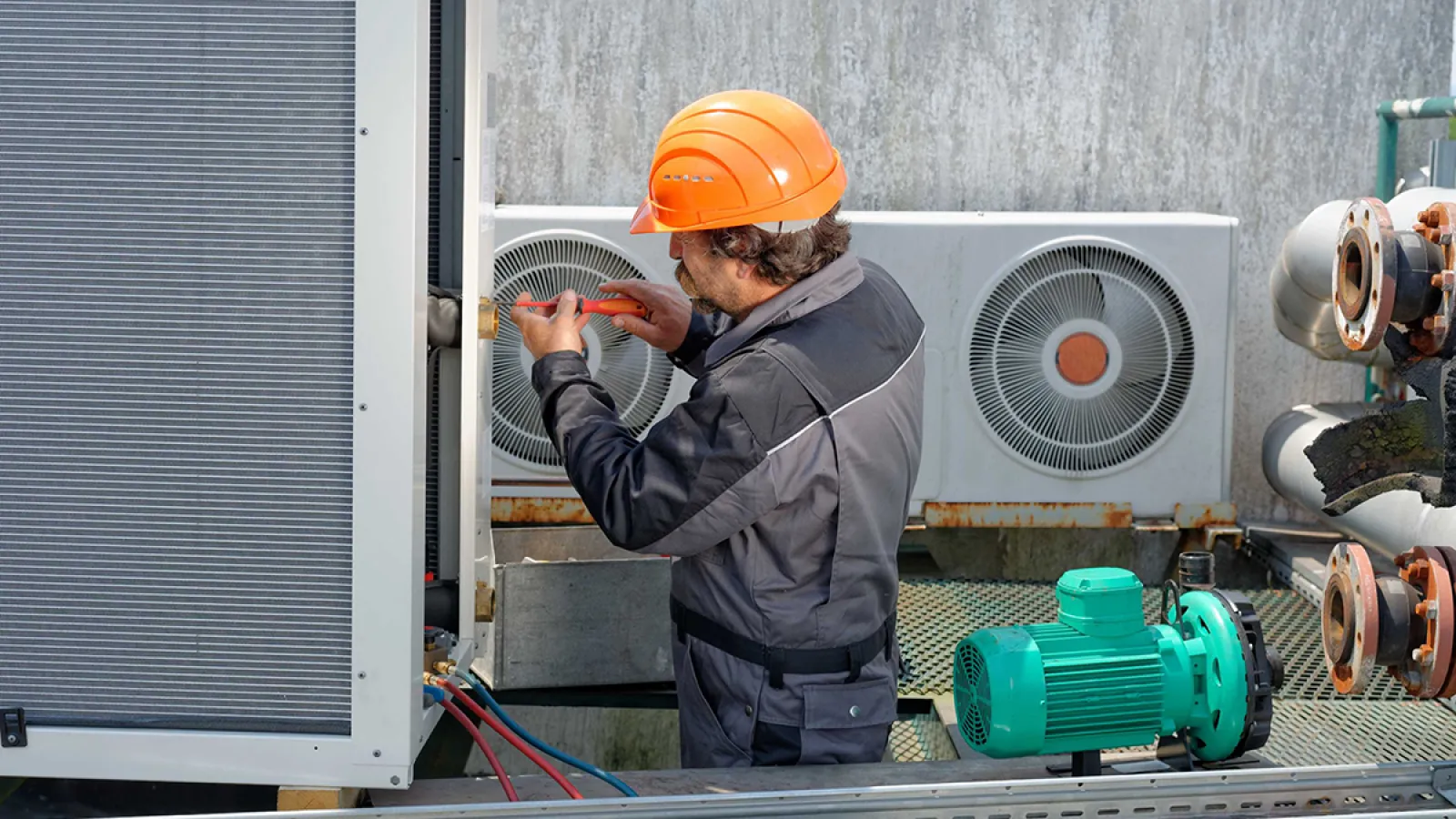 Technician in orange helmet repairing industrial HVAC unit by adjusting system components outdoors