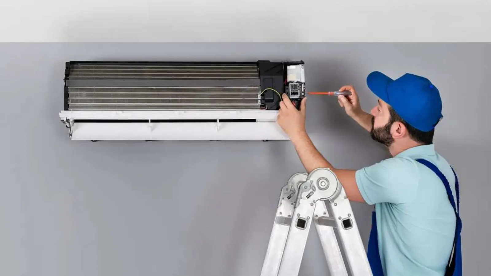 Technician with glasses inspecting and repairing an outdoor HVAC unit during daytime.