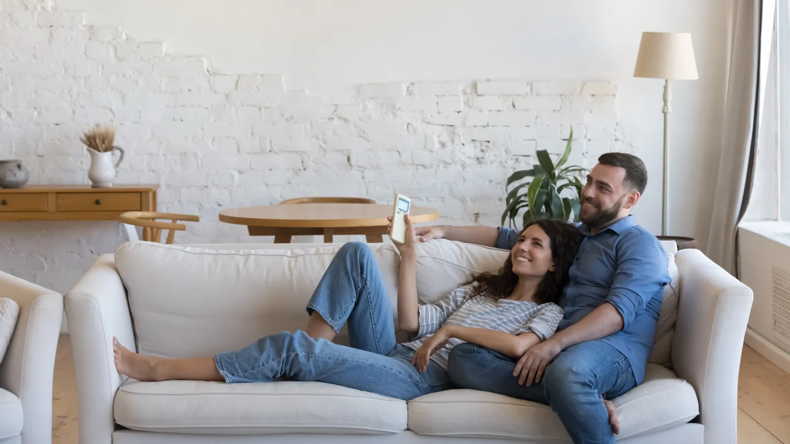 Couple relaxing on a white sofa in a bright living room with air conditioner and natural light