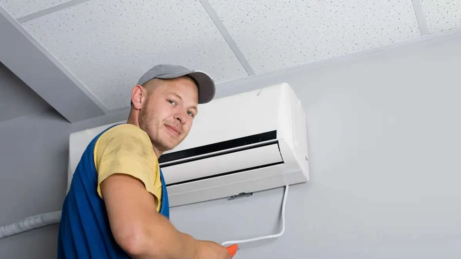 Technician with glasses inspecting and repairing an outdoor HVAC unit during daytime.