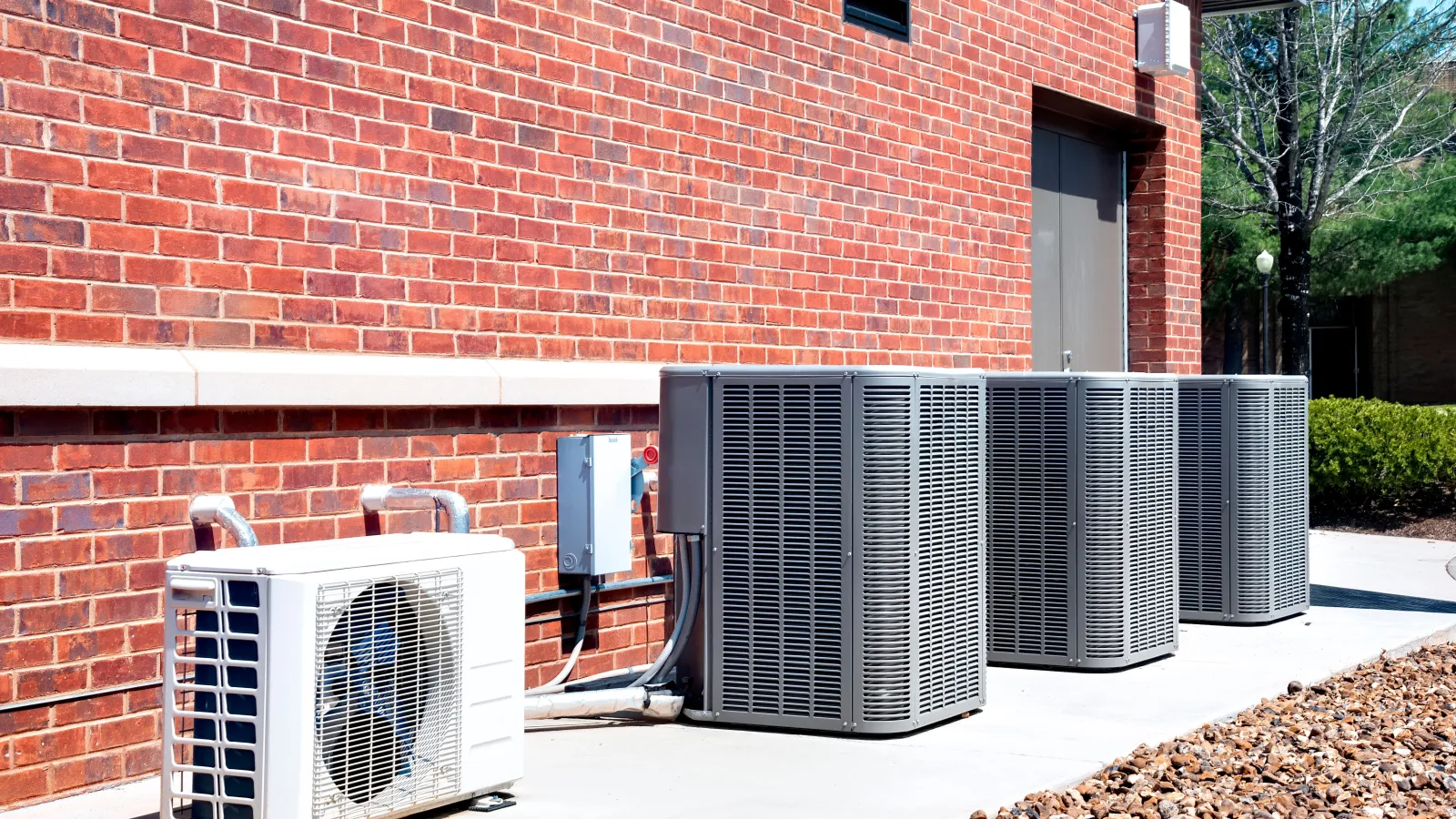 Outdoor air conditioning units installed on a concrete pad beside a red brick building on a sunny day