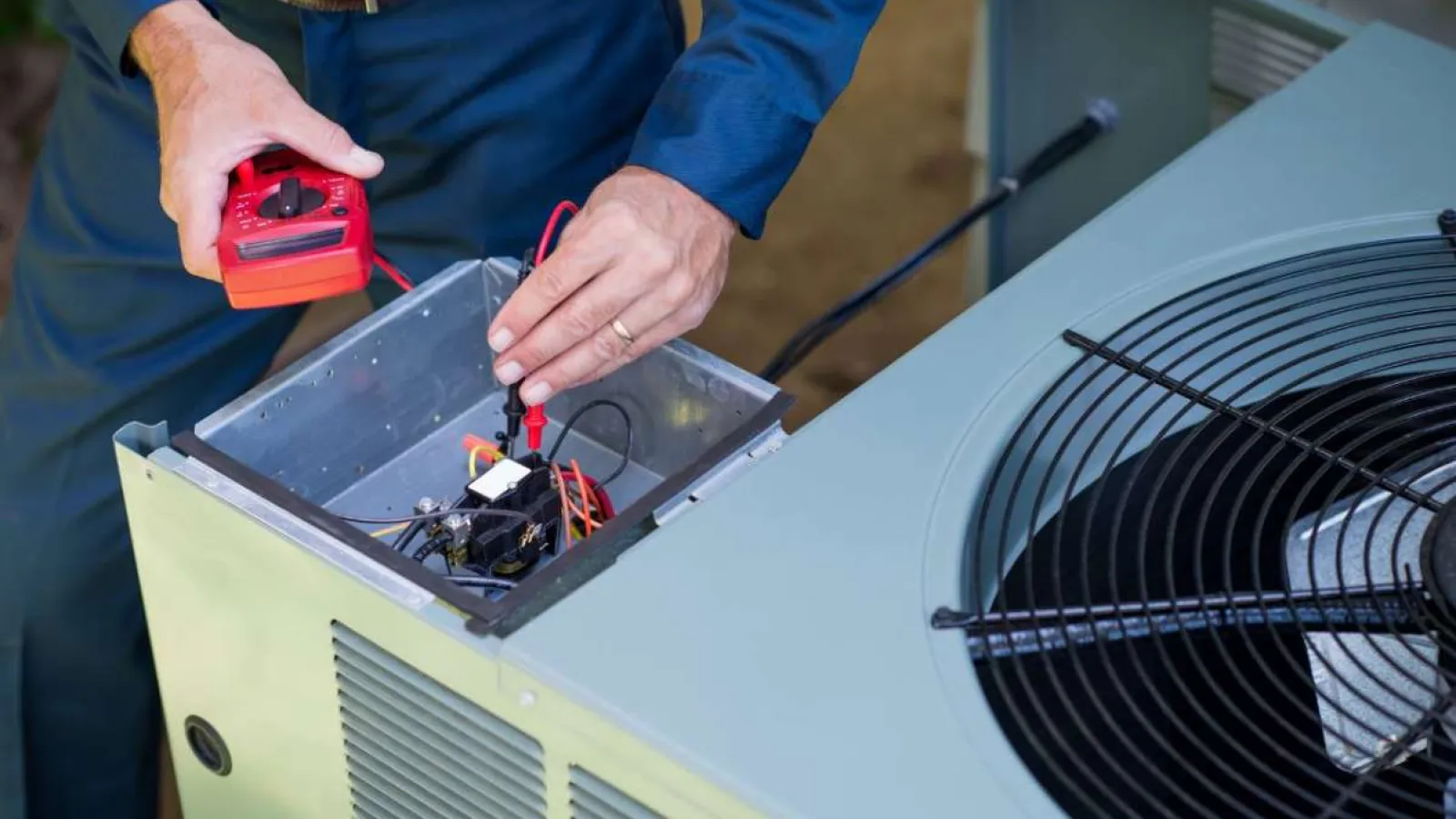 Technician using multimeter to check wiring inside an air conditioning unit during HVAC maintenance.