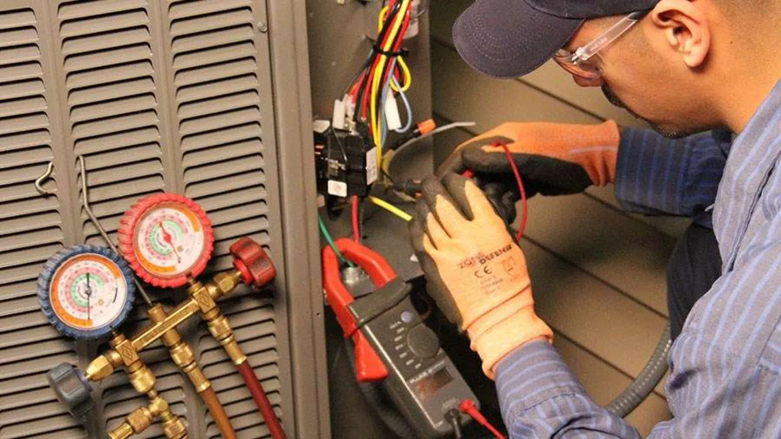 Technician with glasses inspecting and repairing an outdoor HVAC unit during daytime.