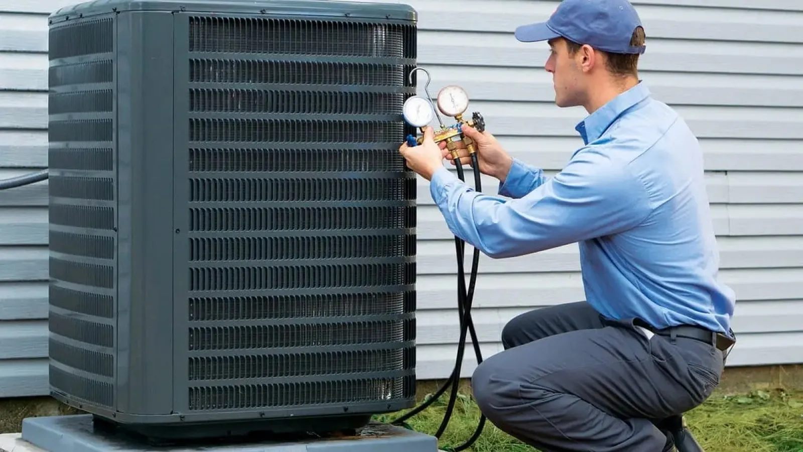 Technician in blue uniform inspecting outdoor air conditioning unit with gauges and tool bag on grass.