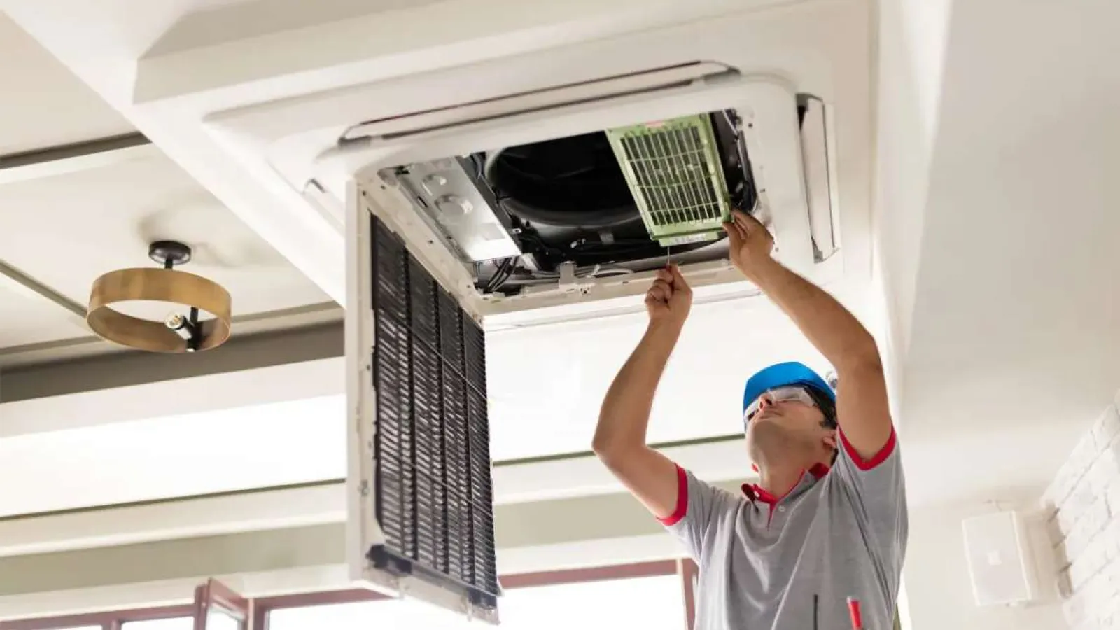 Technician with glasses inspecting and repairing an outdoor HVAC unit during daytime.