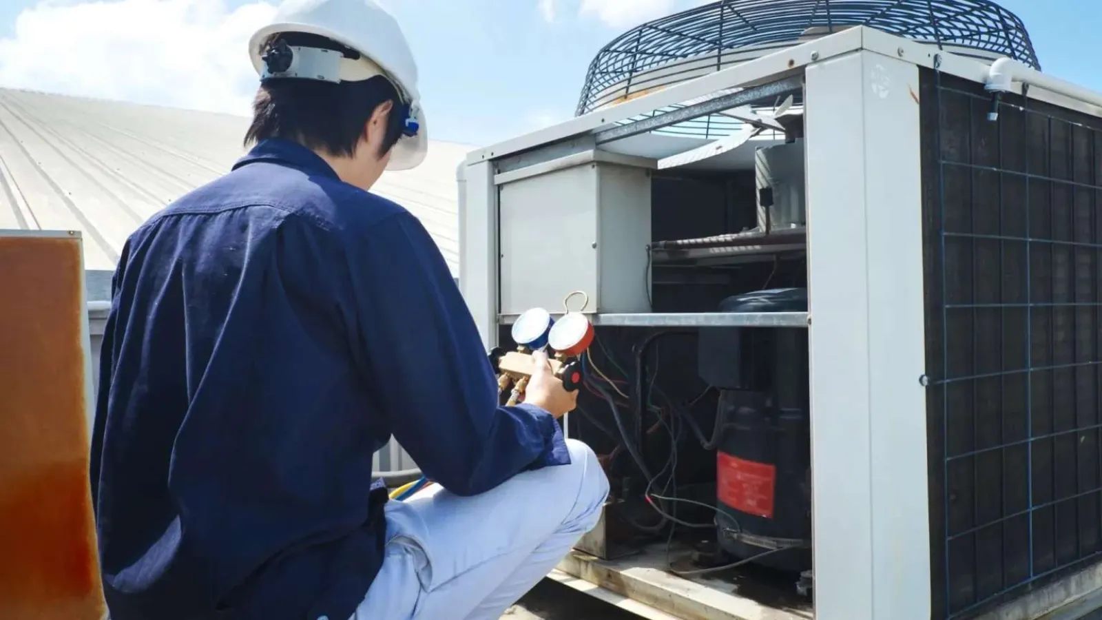Technician with glasses inspecting and repairing an outdoor HVAC unit during daytime.