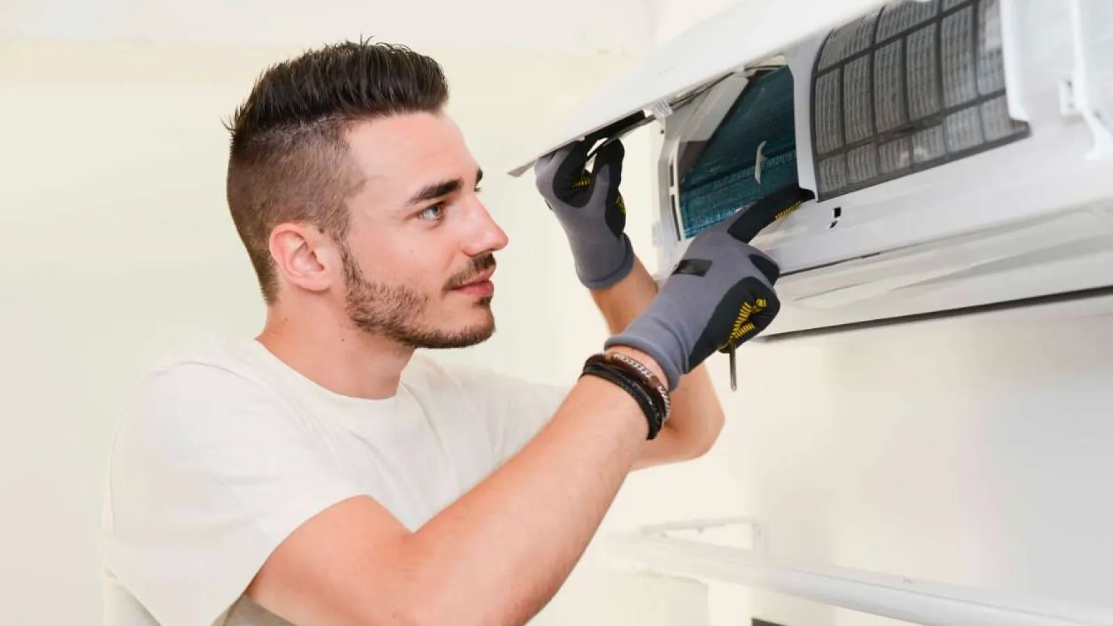 Technician with glasses inspecting and repairing an outdoor HVAC unit during daytime.