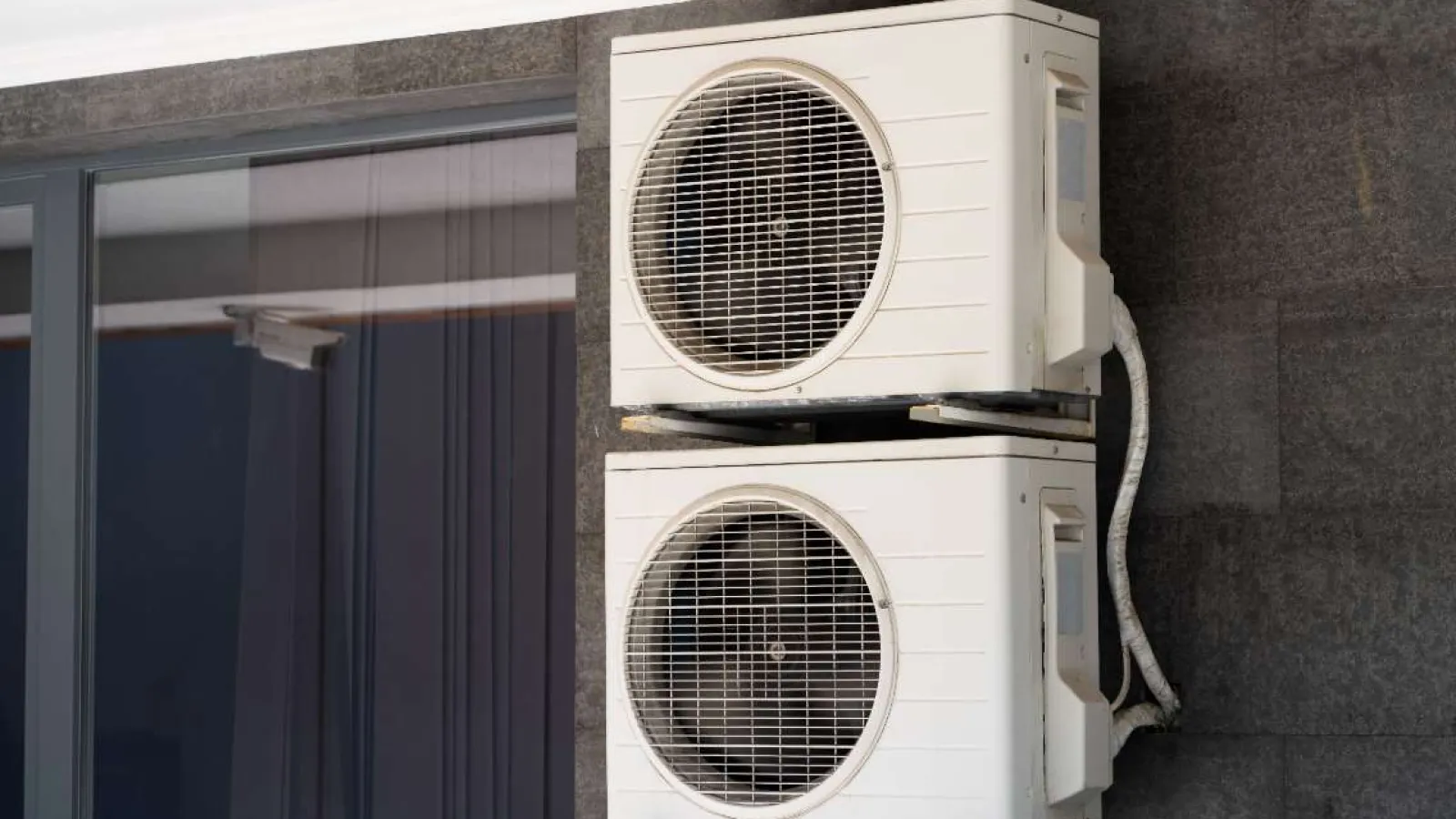 Technician with glasses inspecting and repairing an outdoor HVAC unit during daytime.