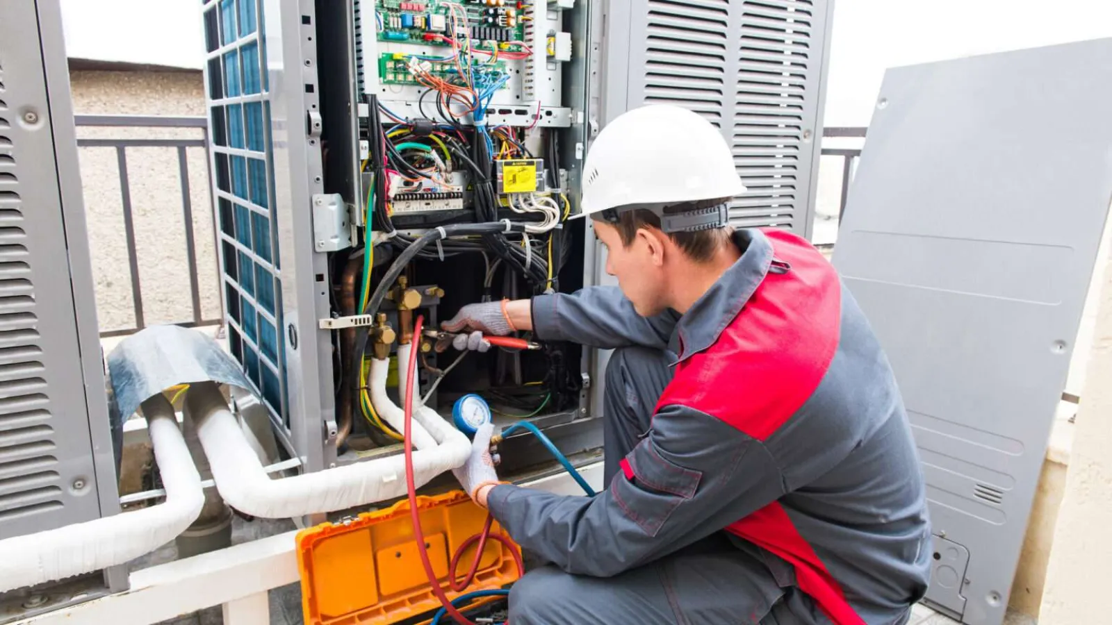 Technician with glasses inspecting and repairing an outdoor HVAC unit during daytime.