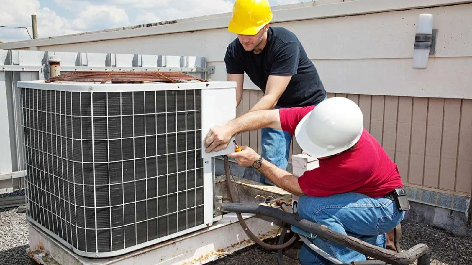 Technician with glasses inspecting and repairing an outdoor HVAC unit during daytime.