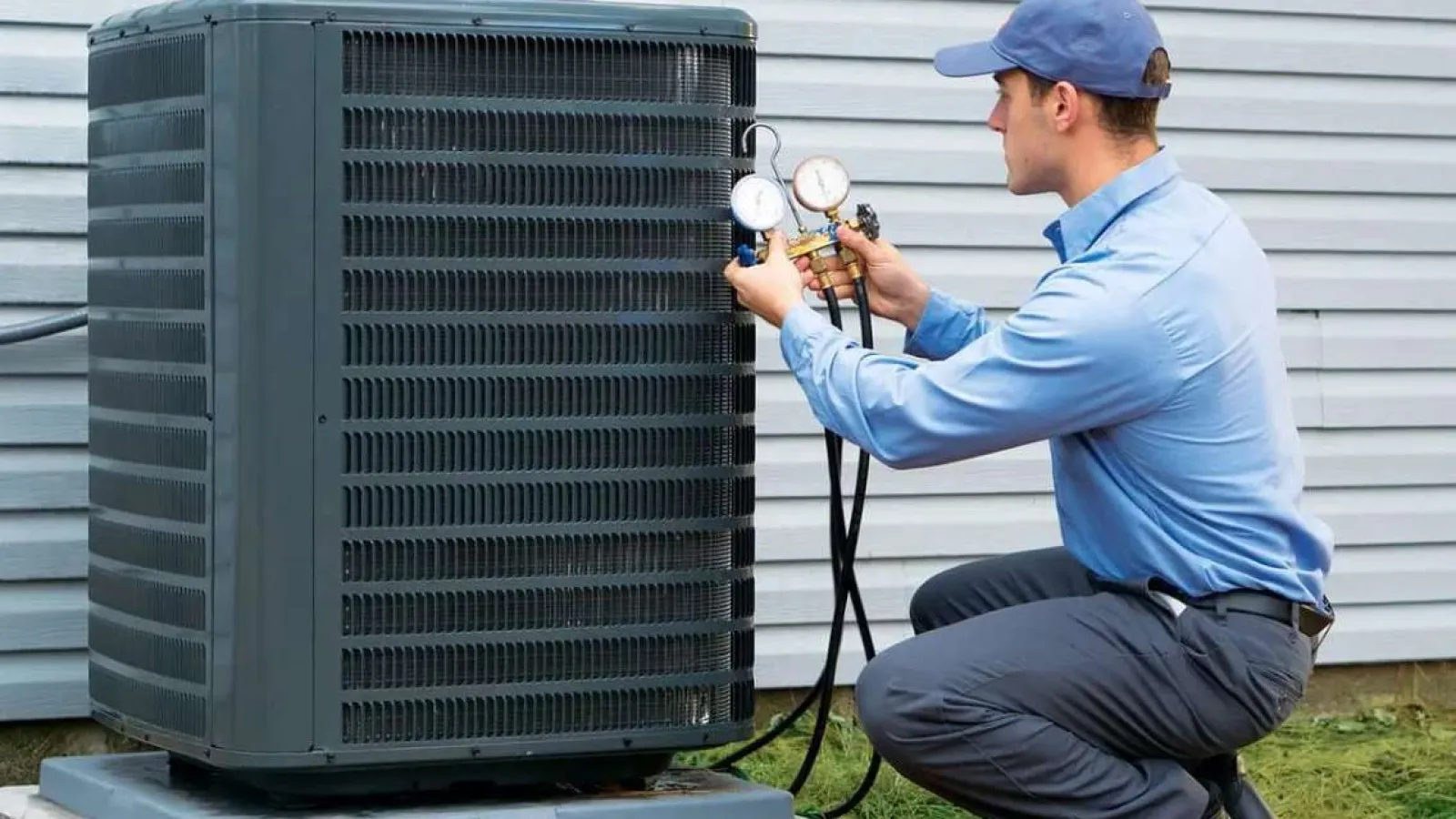 Technician with glasses inspecting and repairing an outdoor HVAC unit during daytime.
