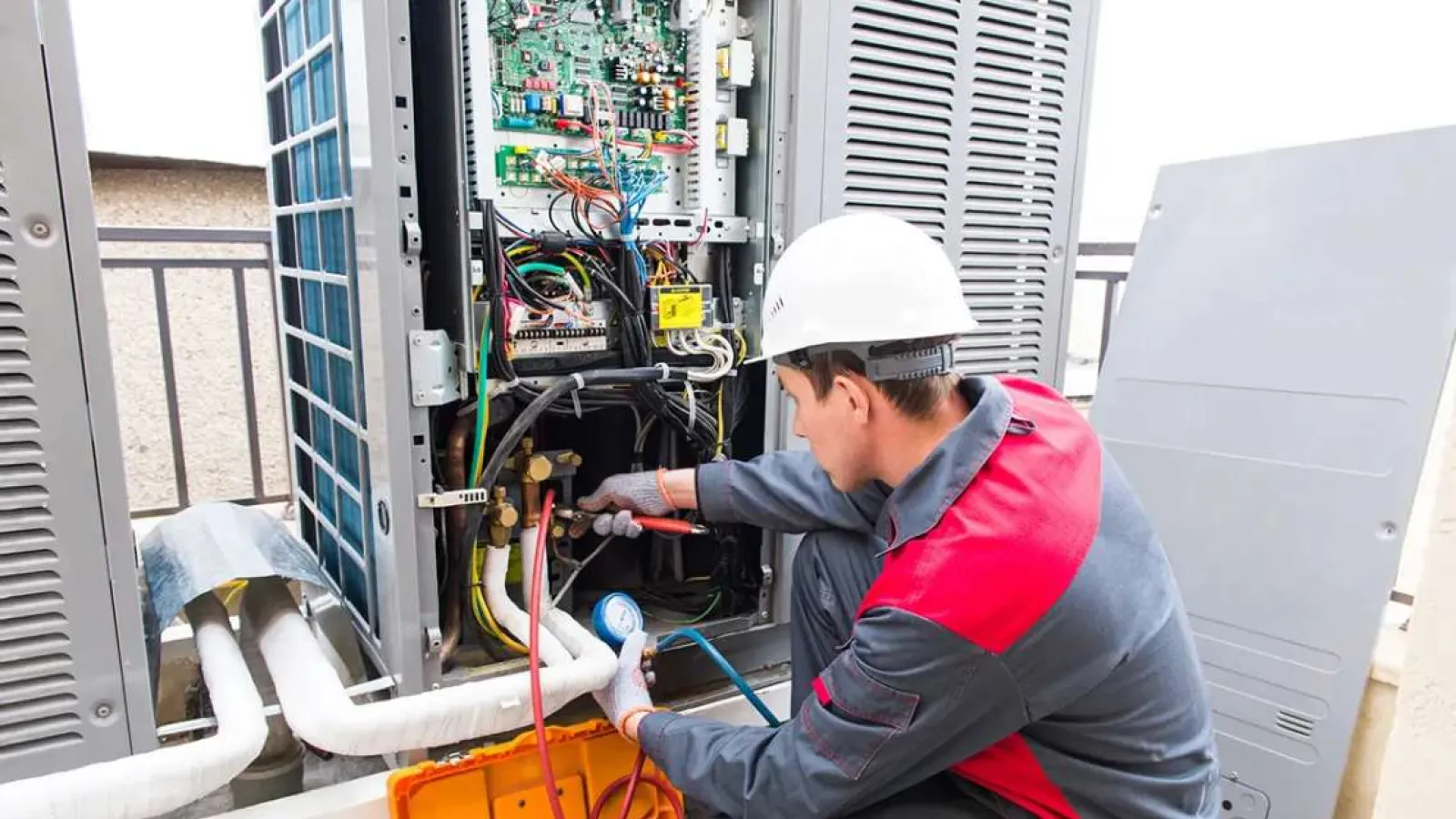 Technician in safety helmet repairing and checking outdoor HVAC air conditioning system with tools