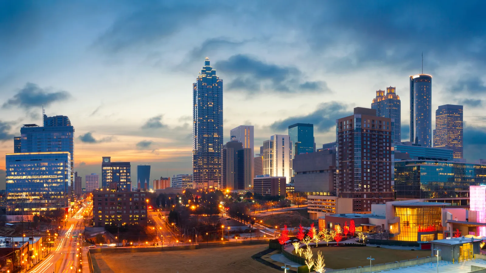 Atlanta city skyline at dusk with illuminated buildings and streets under a cloudy sky.