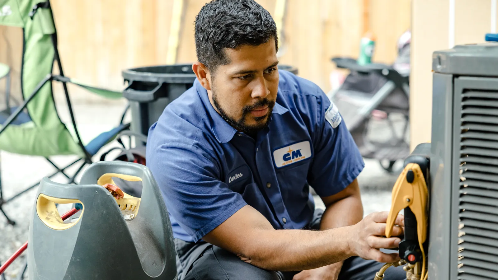 Technician in blue uniform repairing an air conditioning unit outdoors using gauges and hoses for pressure testing
