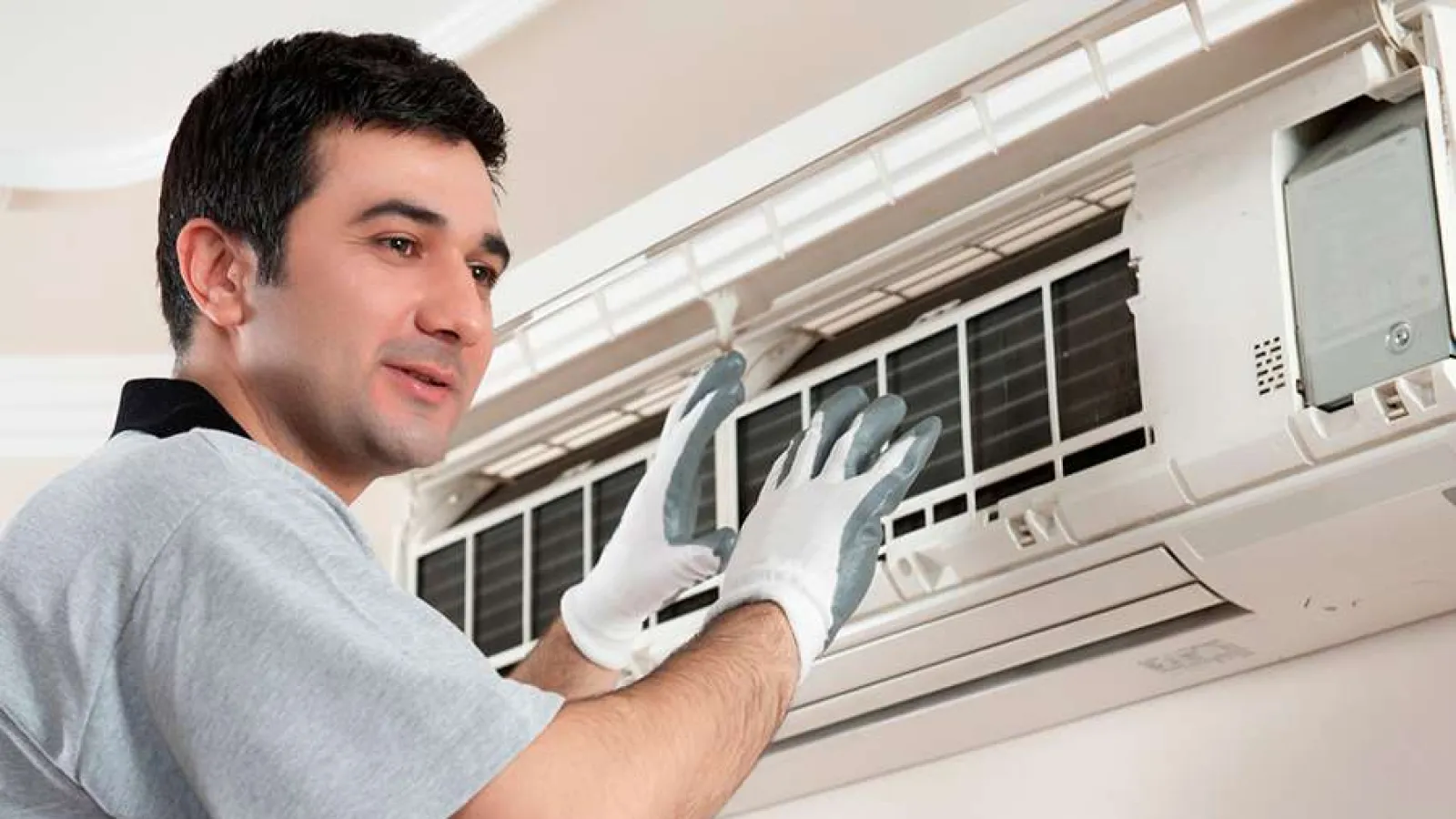 Technician wearing gloves servicing an indoor wall-mounted air conditioning unit for maintenance or repair work.