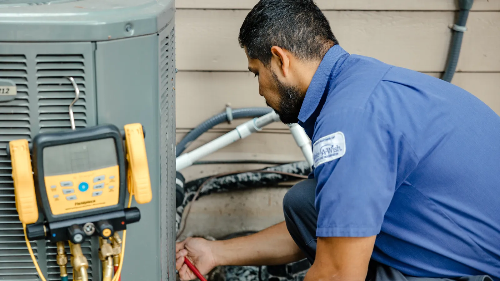 HVAC technician in blue uniform inspecting and repairing outdoor air conditioning unit with diagnostic tools.
