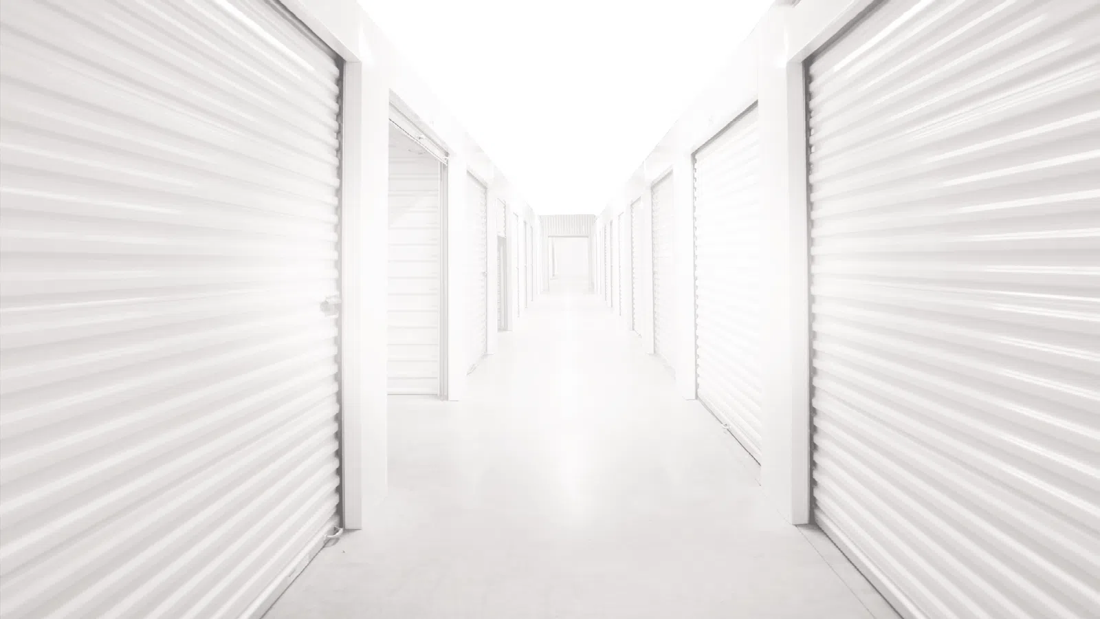 Bright white corridor with closed white metal storage unit doors on both sides in a storage facility.