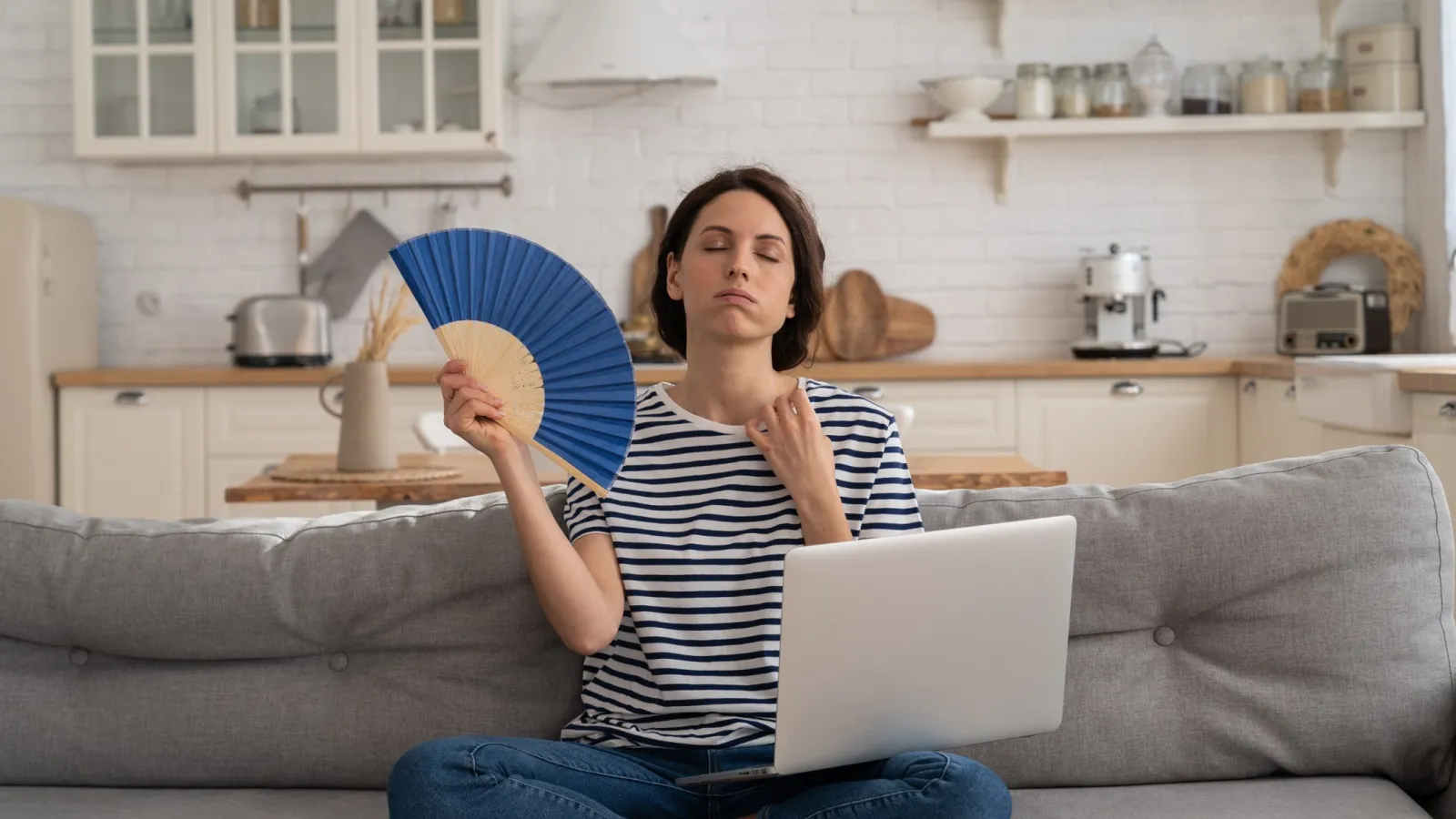 a woman sitting on a couch holding a plate and a laptop in need of ac repair