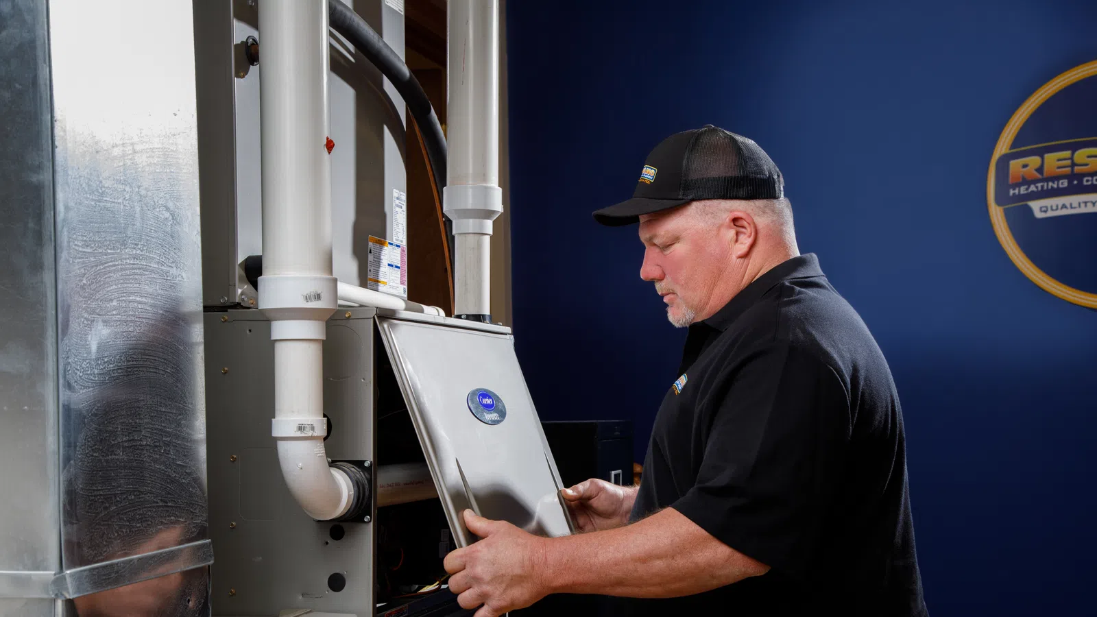 Technician inspecting a heating system, with a blue wall background and HVAC equipment visible.