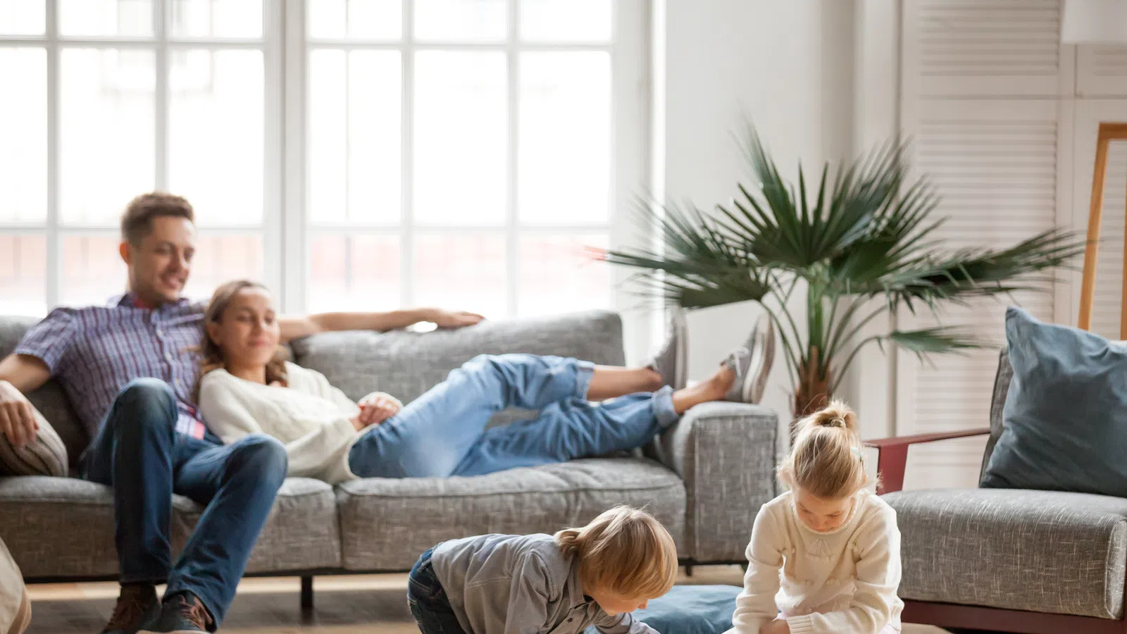 Family enjoying time together at home; children drawing while parents relax on the sofa.