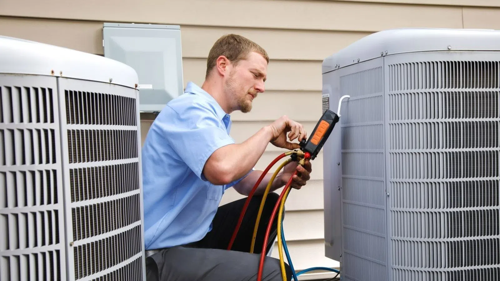 Technician inspecting and adjusting outdoor air conditioning units with gauges and hoses for HVAC maintenance.