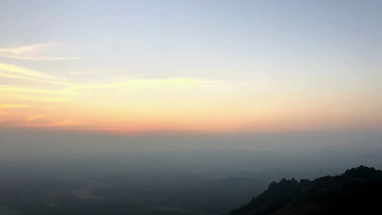 Sunset over misty mountains with soft orange and blue hues blending into a calm evening sky.