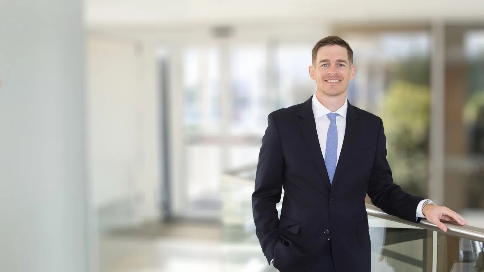 Smiling businessman in navy suit and blue tie standing in bright modern office lobby