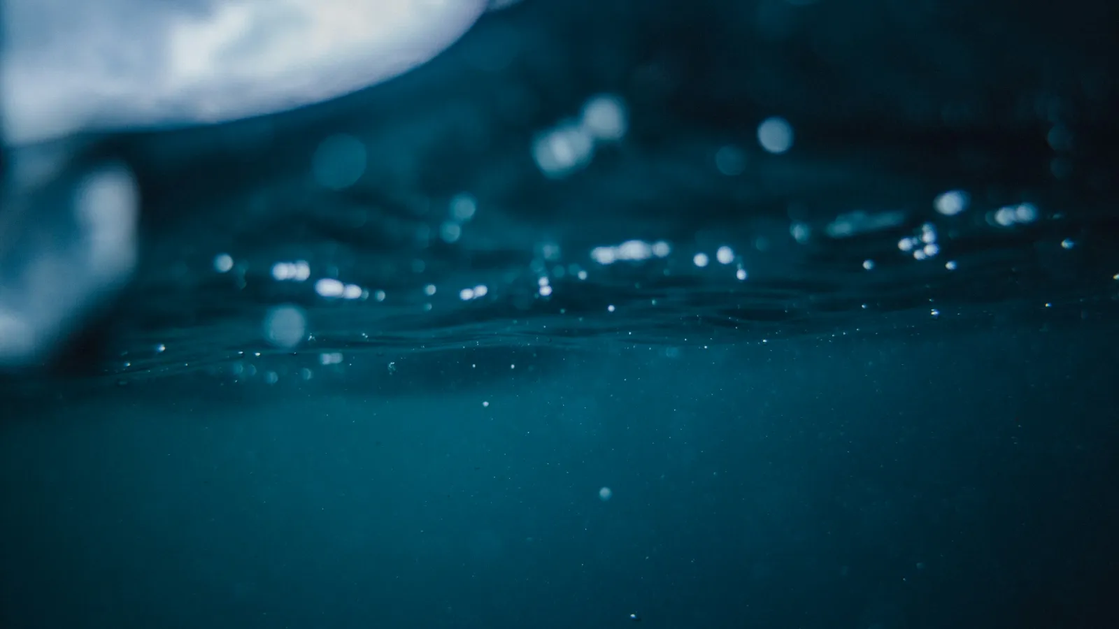 Underwater view showing bubbles and light filtering through dark blue water surface.