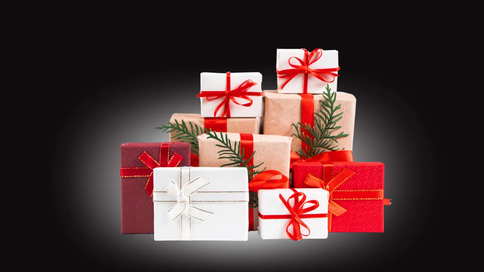 Stack of red, white, and brown Christmas gift boxes with red ribbons and green pine sprigs on black background
