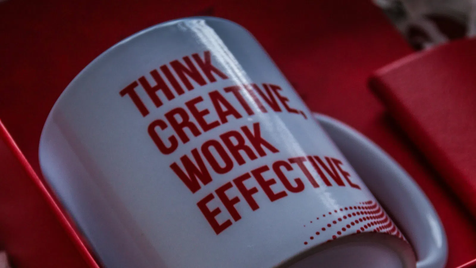 White mug with red text 'Think Creative Work Effective' inside a red gift box with shredded paper.