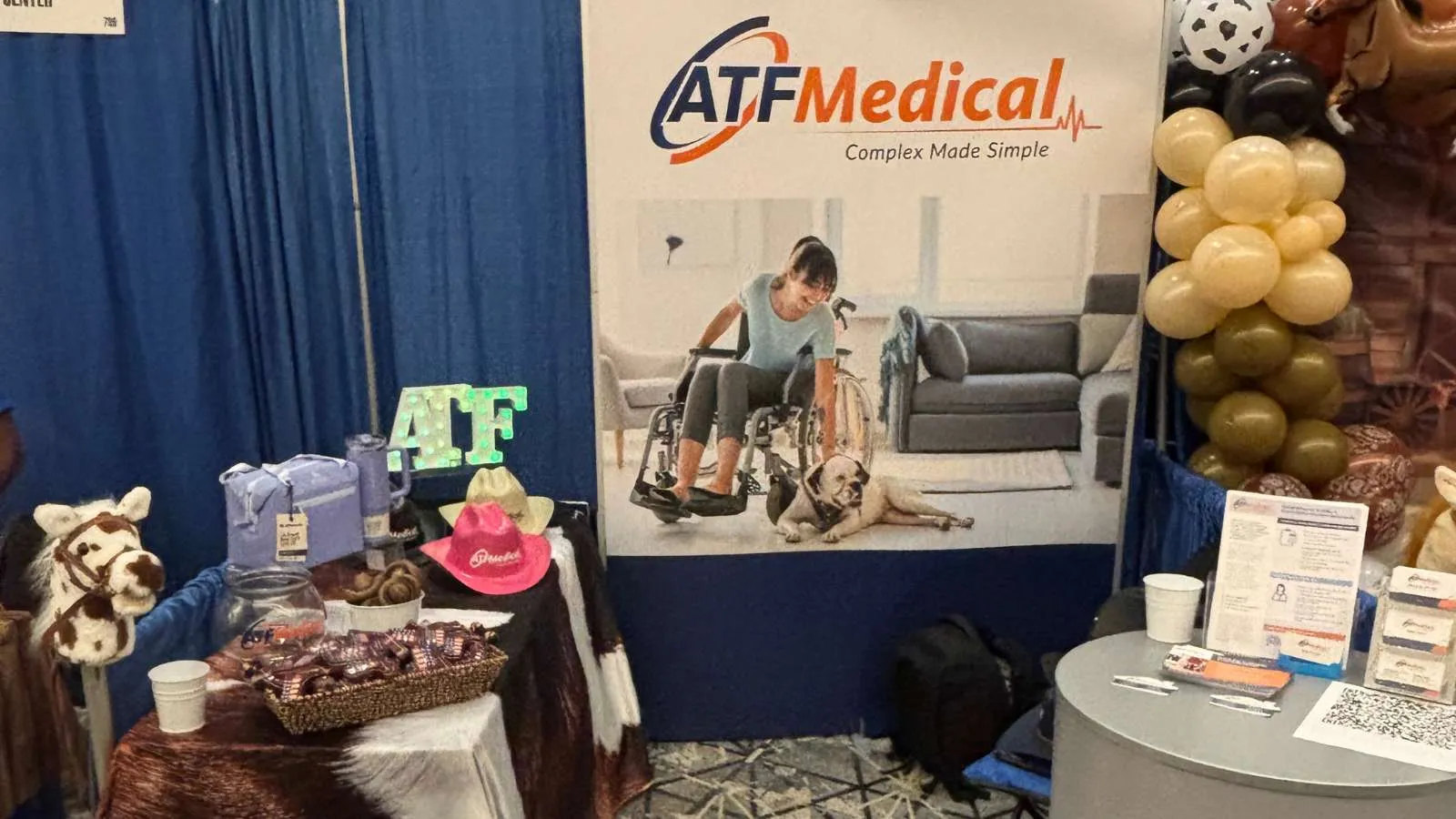 ATF Medical booth with a banner featuring a woman in a wheelchair and promotional items on a decorated table.