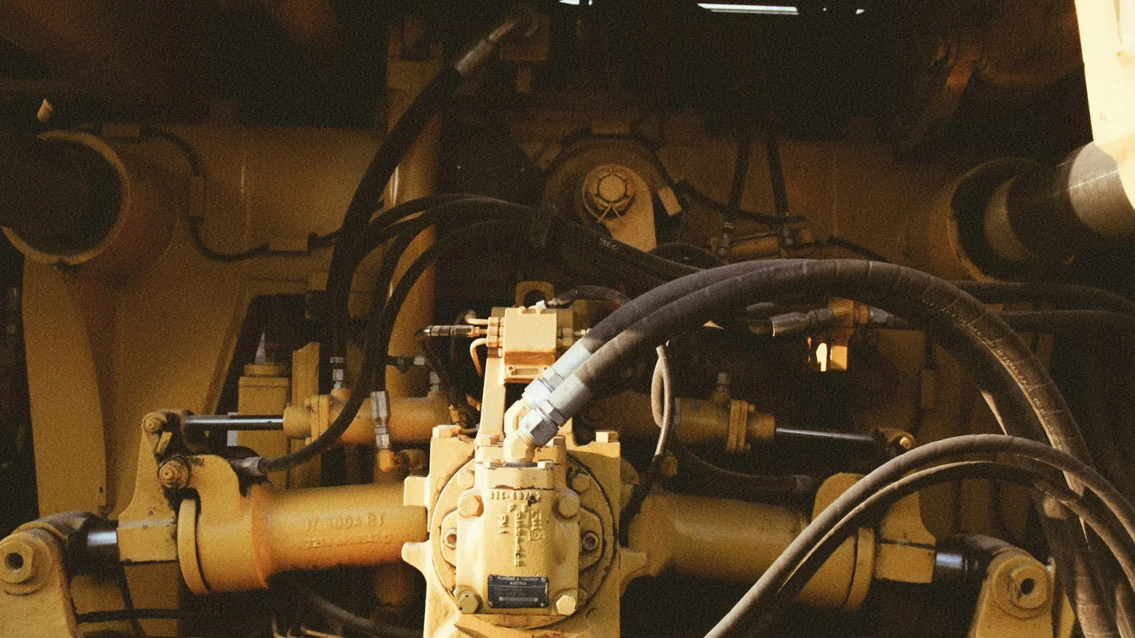 Close-up of hydraulic system with hoses and metal components on heavy machinery in yellow and black.