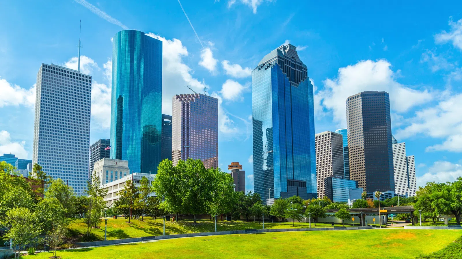 Houston skyline with modern skyscrapers under a bright blue sky and green park in the foreground