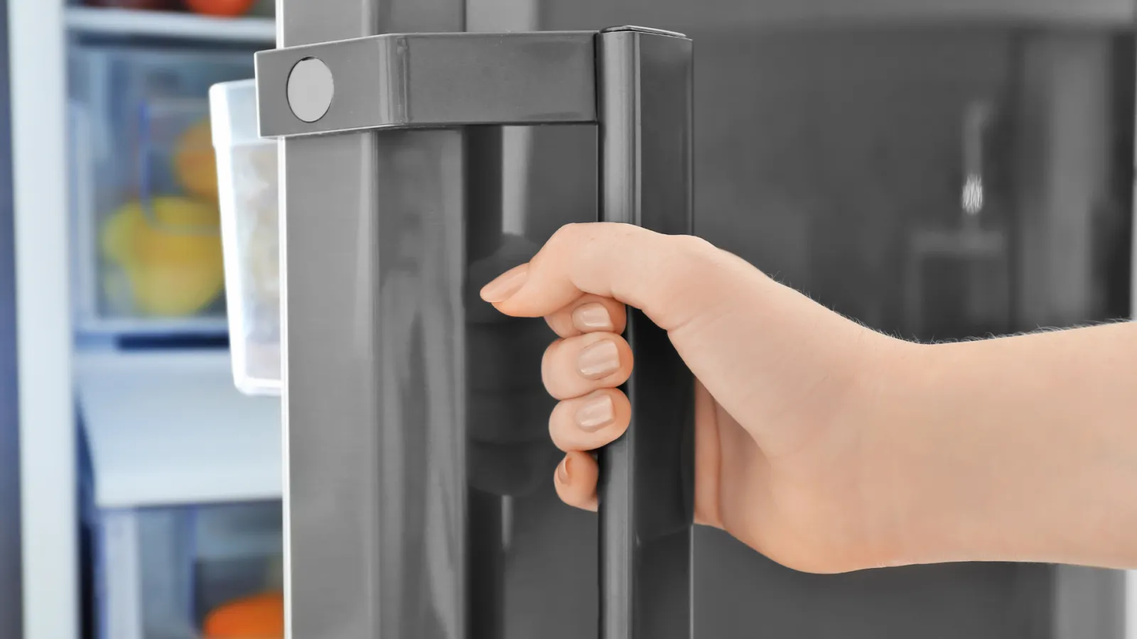 Hand opening stainless steel refrigerator door with visible fresh fruits inside the fridge.
