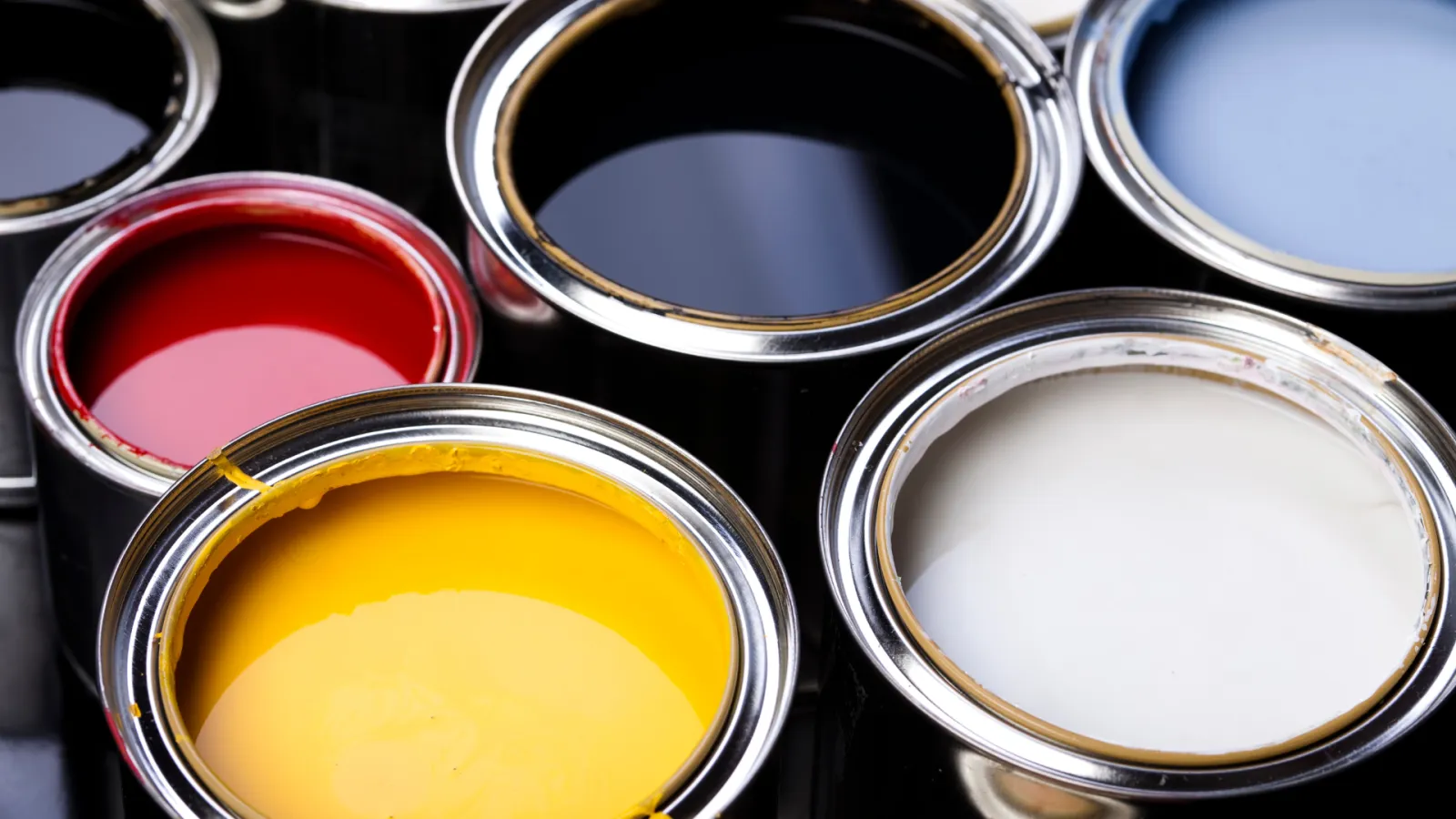 Open paint cans filled with vibrant red, yellow, white, black, and blue colors ready for use.