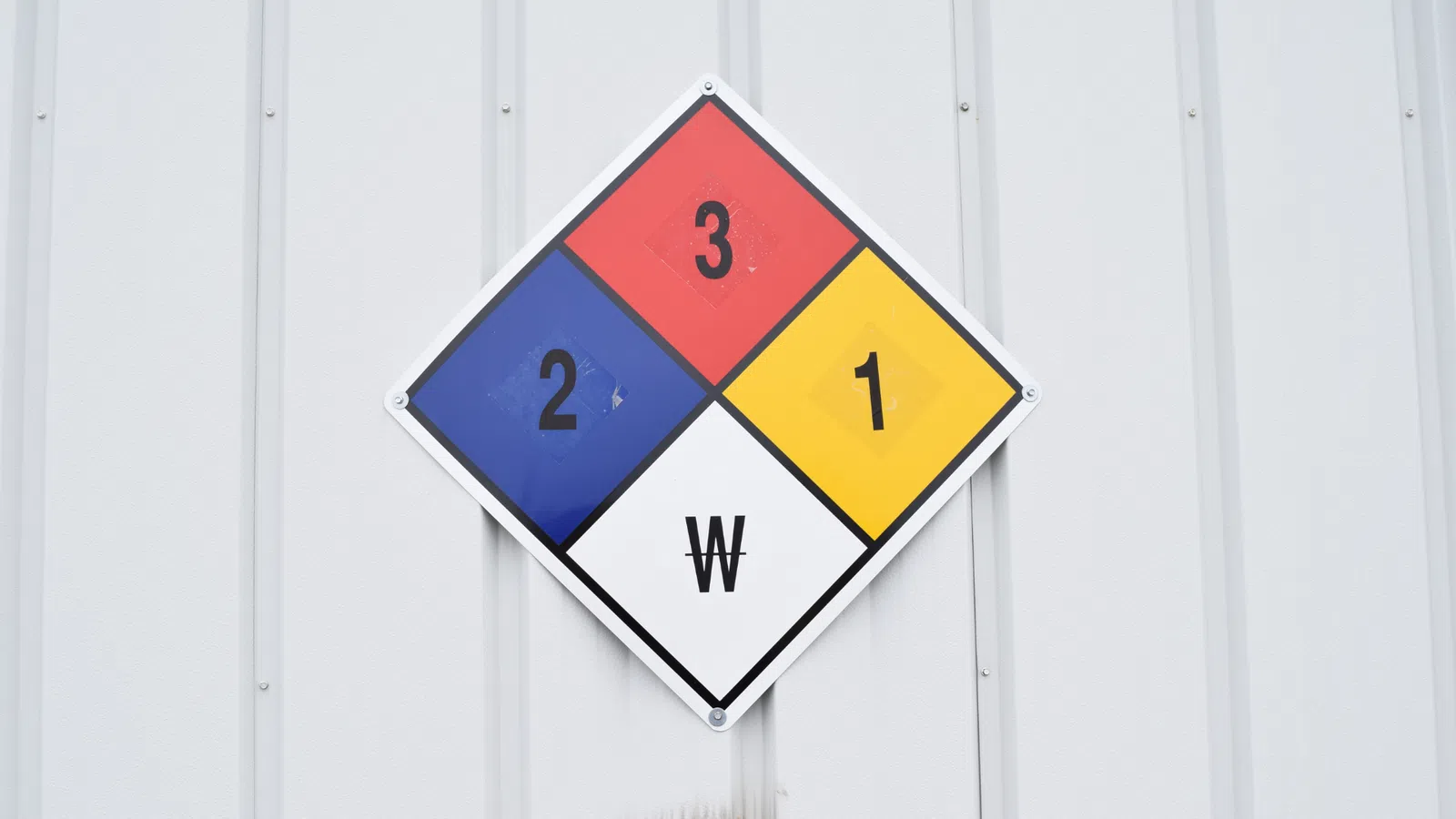 Hazard diamond sign showing danger levels with numbers and a white W symbol on a metal wall.