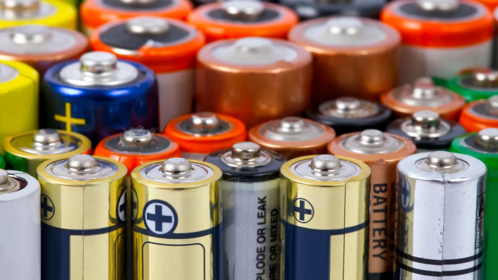 Close-up of assorted AA and AAA batteries with various colored tops and labels tightly packed together.