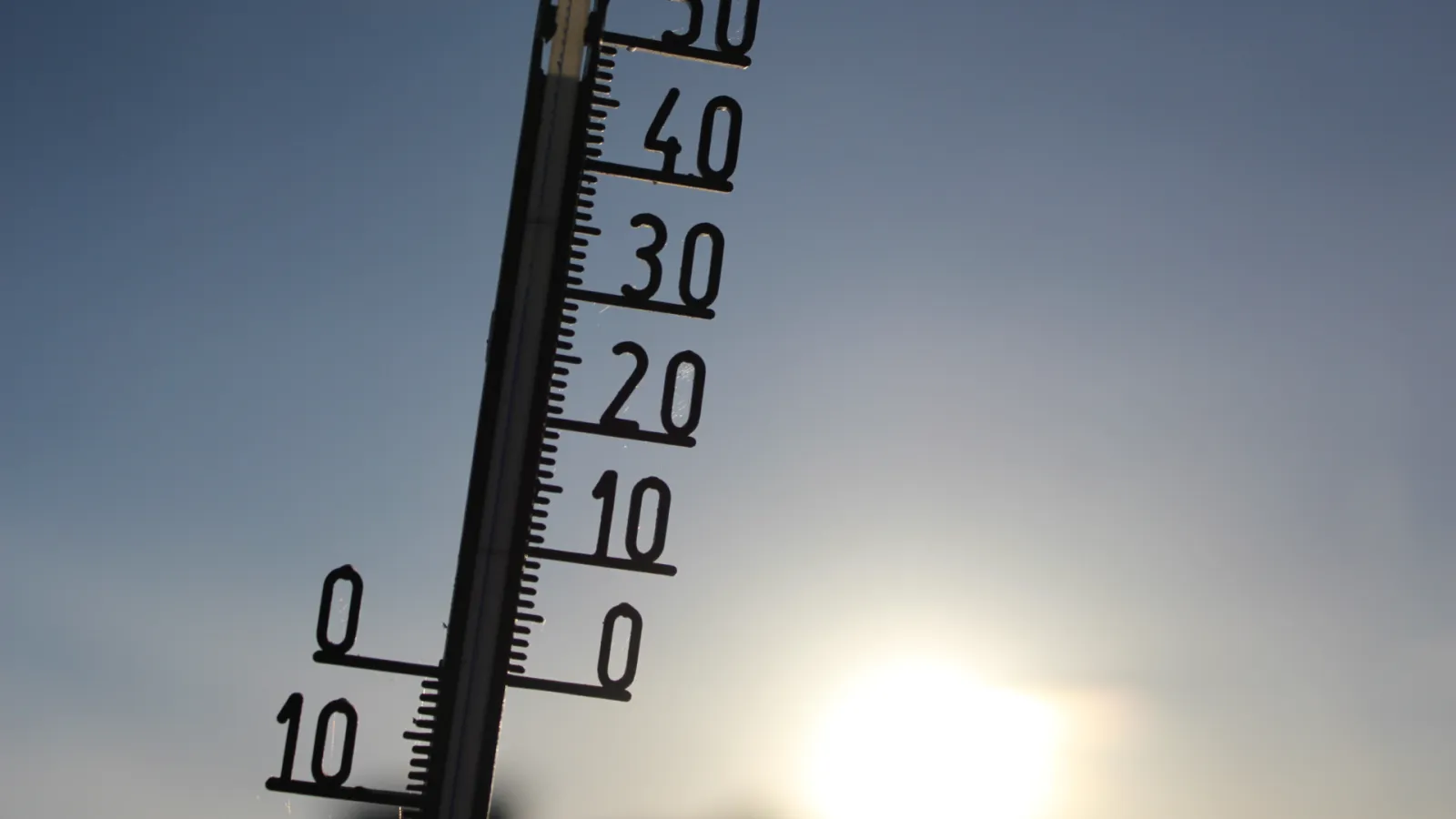 Outdoor thermometer showing temperatures from 0 to 50 degrees against a bright sky with the sun.