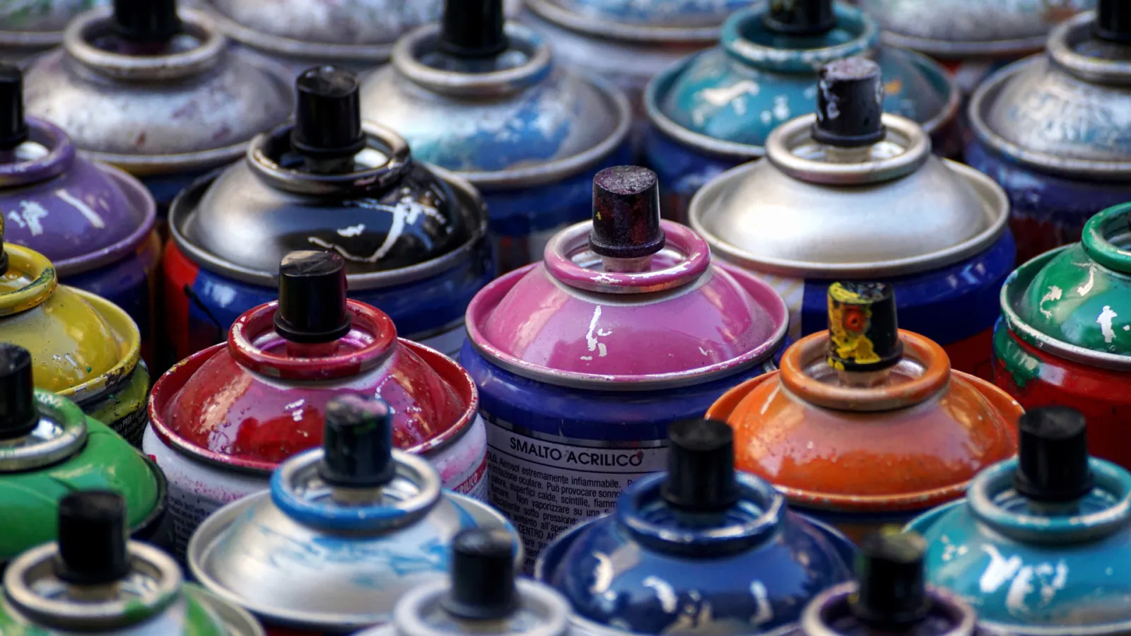 Close-up of various colorful spray paint cans with worn nozzles in an artist's collection
