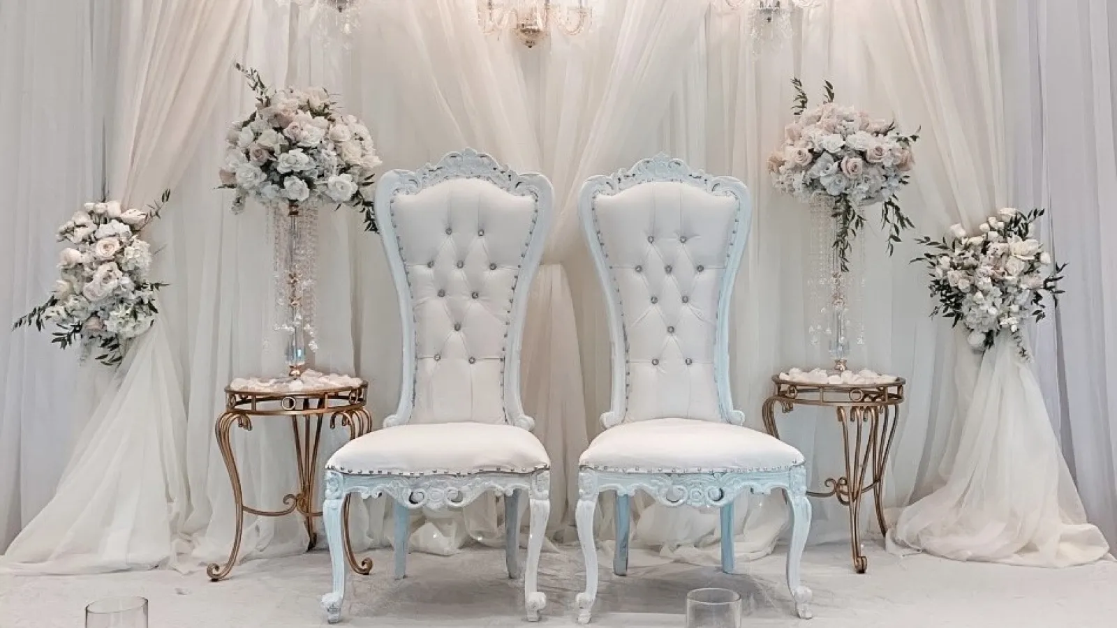 a room with white chairs and a table with glasses and flowers