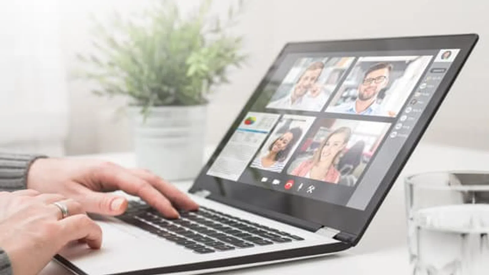 Person typing on laptop during video conference call with four participants visible on screen