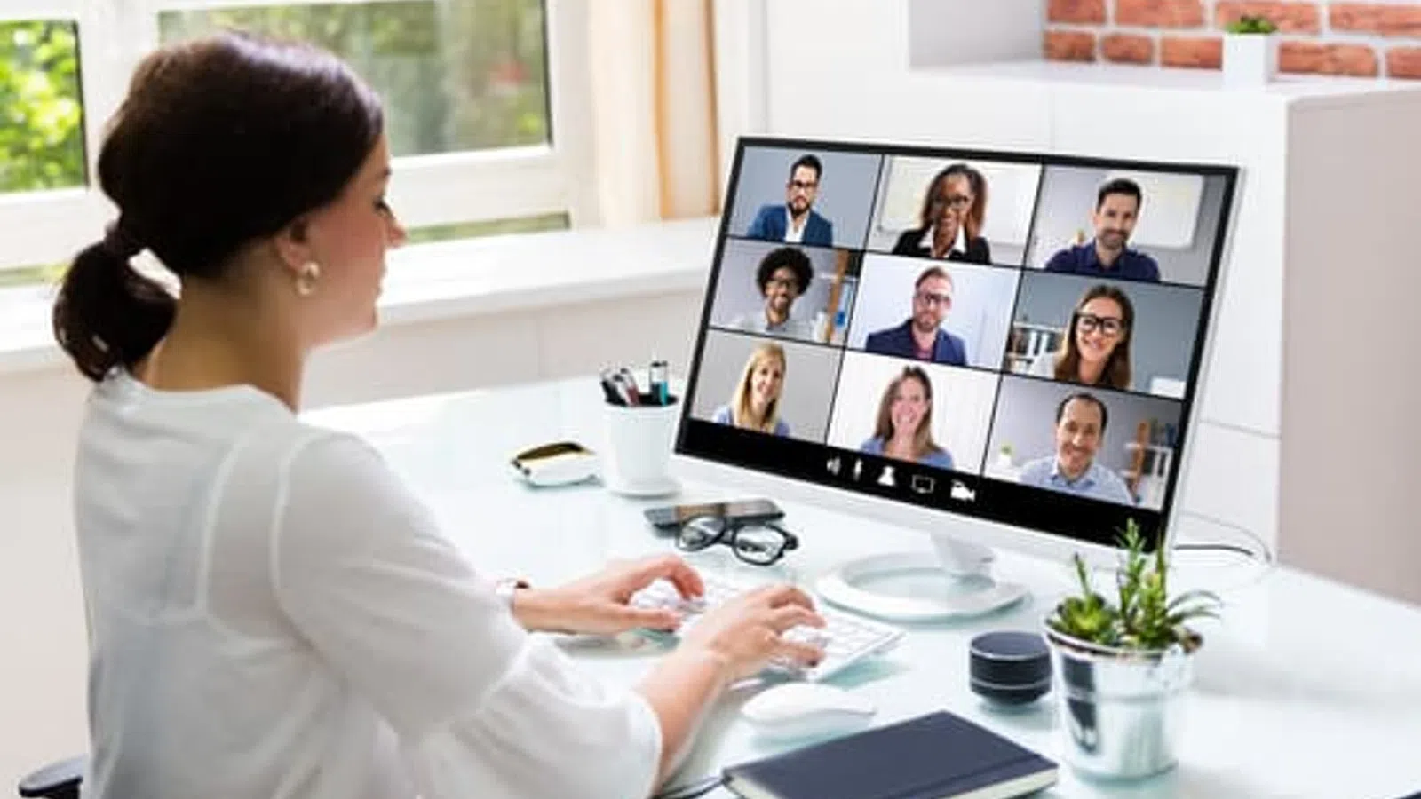 Woman participating in a video conference call with nine colleagues on a desktop computer at home office.