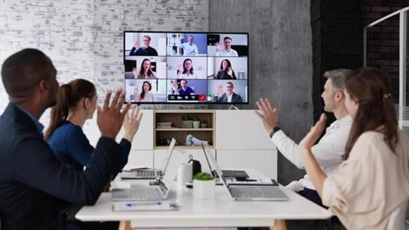 Team of four people participating in a video conference call with multiple colleagues on a large screen